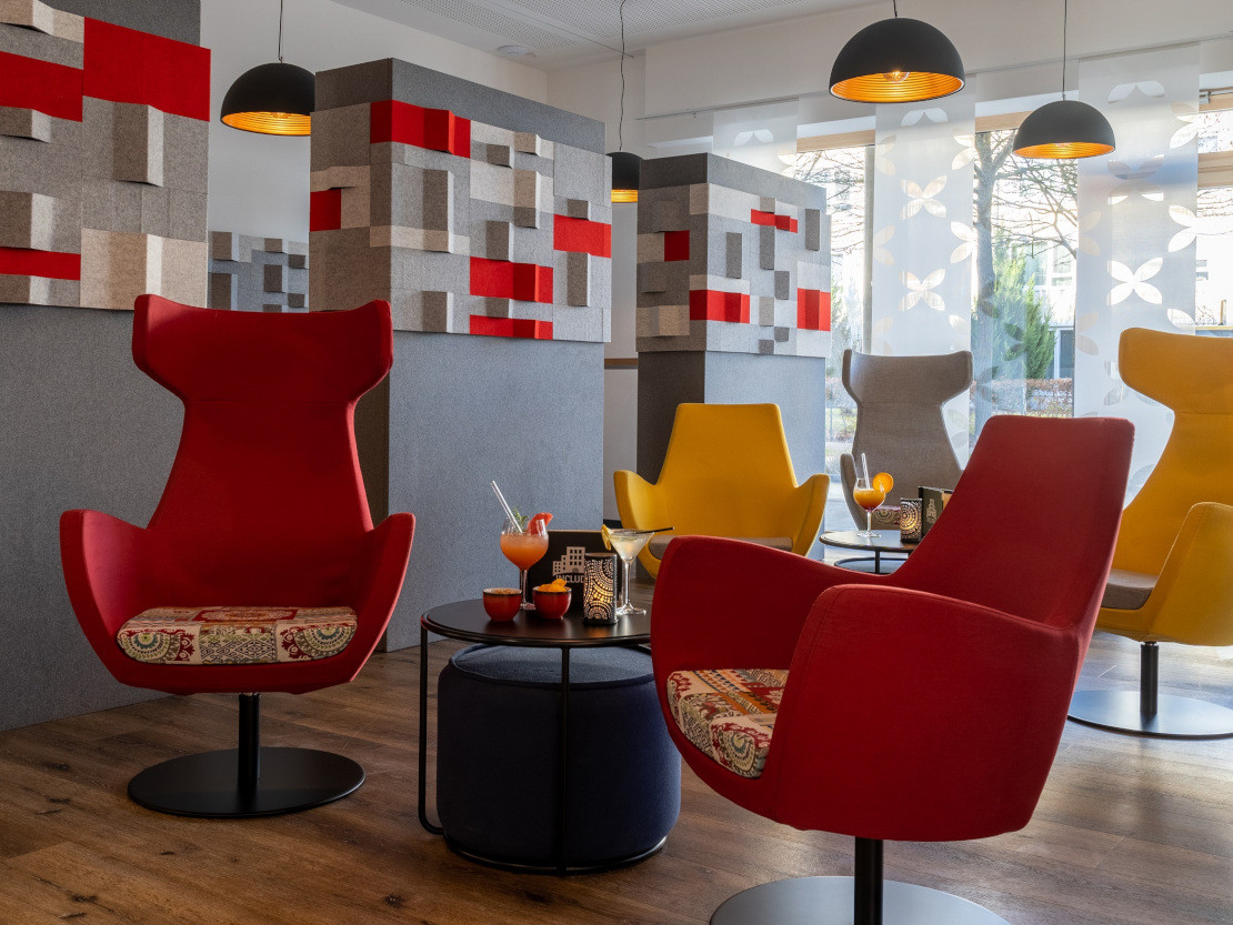 Die Lobby lädt mit gemütlichen Stühlen zum Verweilen ein - Rote und gelbe Sessel verschönern die Lobby des Hotels - © Johanniter-Hotel Regensburg gGmbH